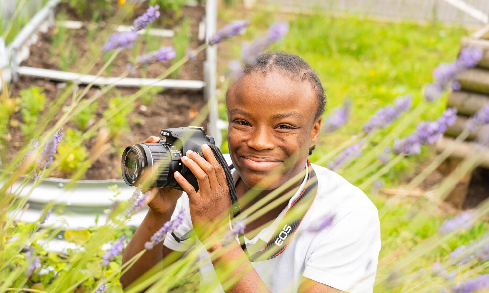 Prospere Learning Trust student holding a camera in a field with grass and flowers.